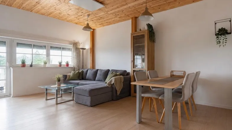Heller Wohn-Essbereich mit Holzbalkendecke, modernem Sofa und Esstisch.