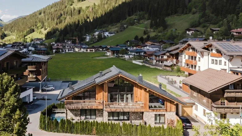 Großzügiges Chalet mit Pool in alpiner Umgebung, umgeben von grünen Hügeln und Bergen.