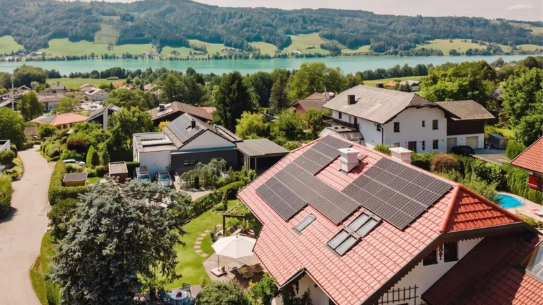 Luftaufnahme eines Wohngebiets mit Häusern, Solaranlagen und einem See im Hintergrund.