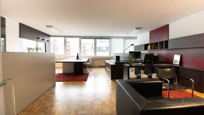 Geräumiges und helles Büro mit mehreren Arbeitsplätzen, Holzparkettboden und großen Fenstern.