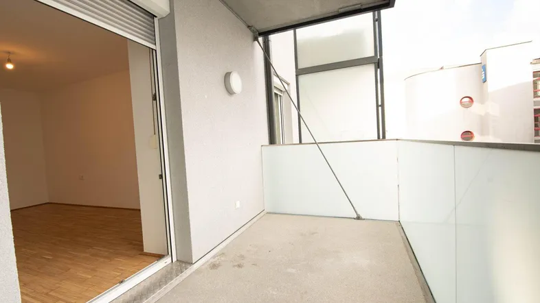 Geräumiger Balkon mit Blick in einen hellen Raum mit Parkettboden, ideal für entspannte Stunden im Freien.