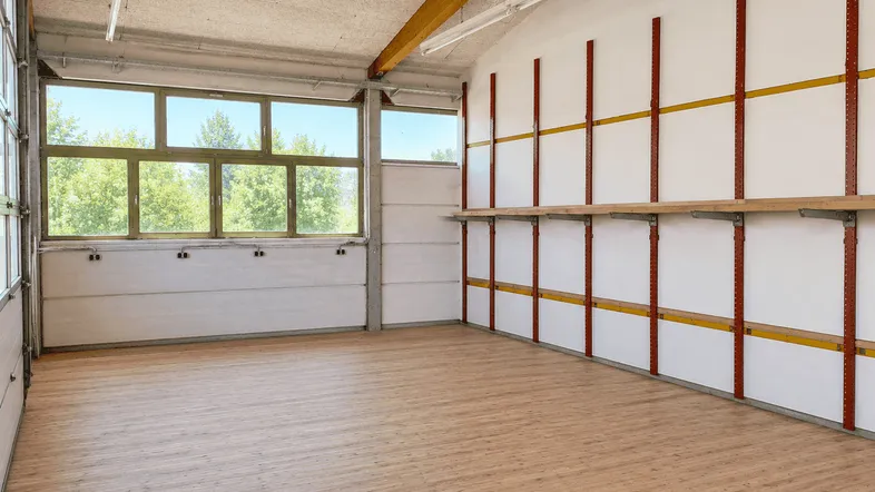 Großer, heller Raum mit Holzboden, großen Fenstern und einem Regalsystem an der Wand.