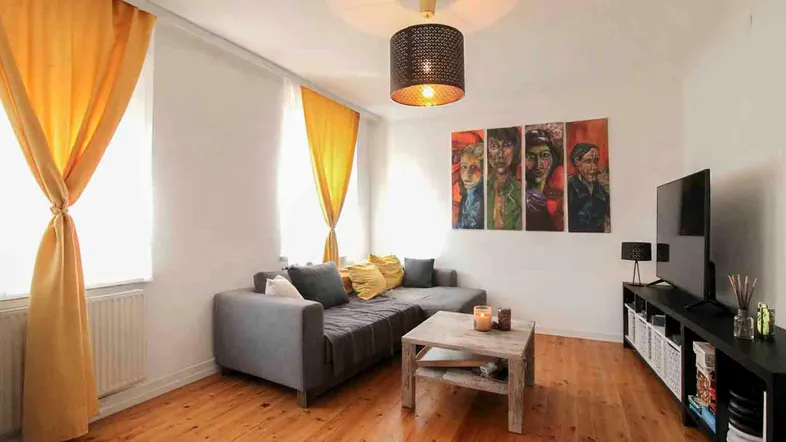 Helles Wohnzimmer mit Holzboden, bequemer Couch und farbenfrohen Vorhängen, ideal zum Entspannen.