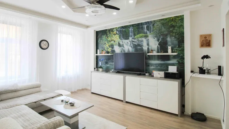 Helles Wohnzimmer mit modernem TV-Möbel, Deckenventilator und dekorativer Wasserfall-Tapete.