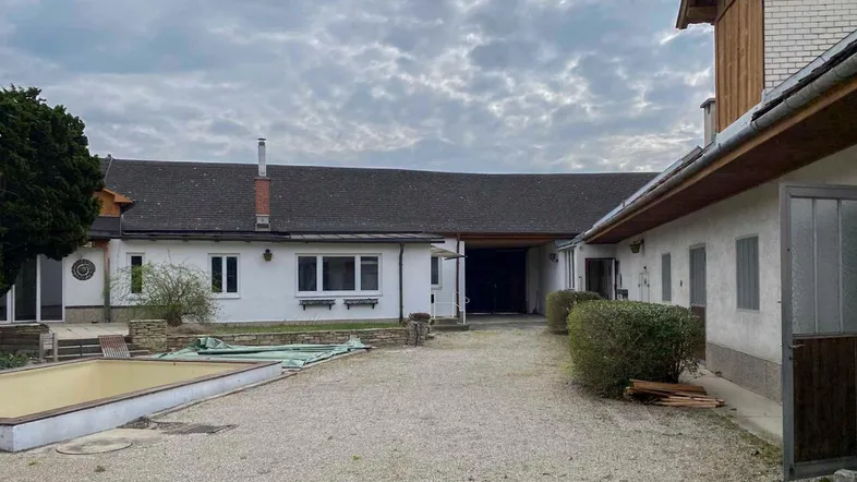 Blick auf den Innenhof mit mehreren Gebäudeteilen und einem leeren Poolbecken unter bewölktem Himmel.