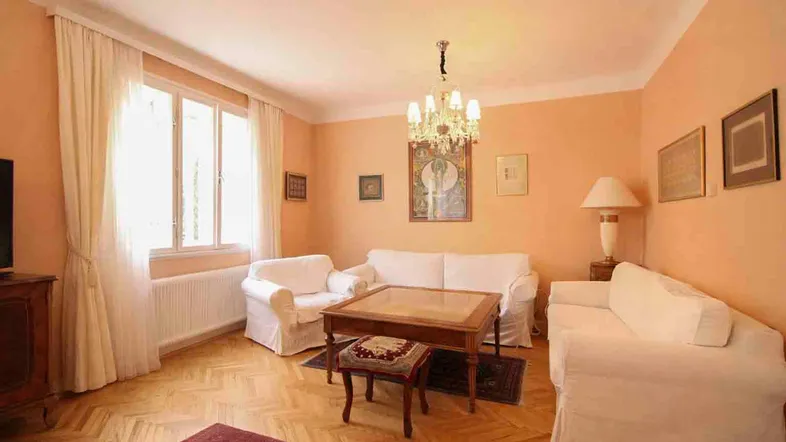 Gemütliches Wohnzimmer mit Parkettboden, hellen Wänden und einem eleganten Kronleuchter.