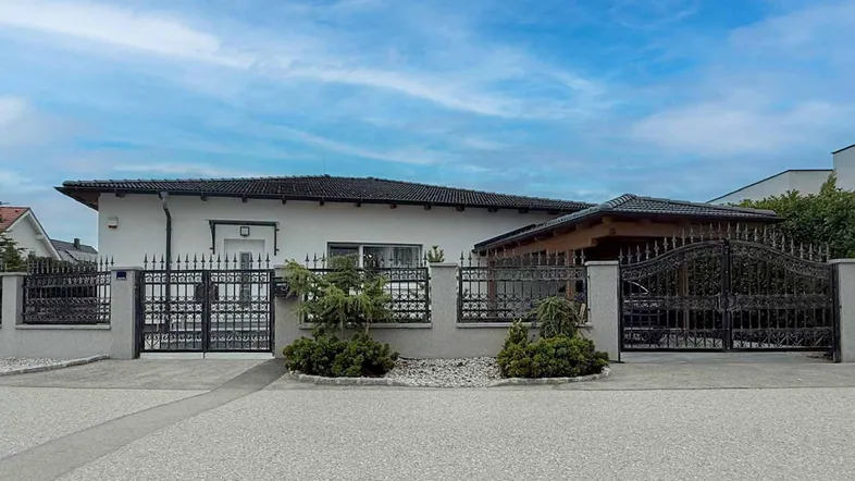 Vorderansicht des Hauses mit schmiedeeisernem Zaun und Einfahrtstor.