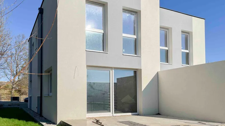 Moderne Neubaufassade mit großen Fenstern und einer kleinen Terrasse im Erdgeschoss.