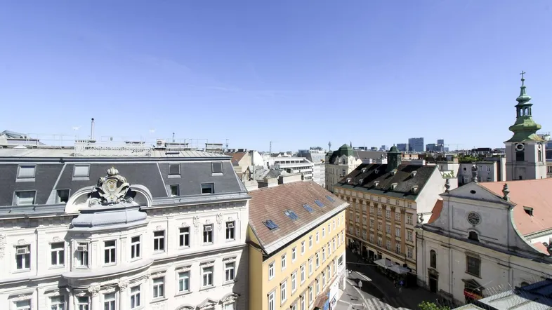 Panoramablick über die Dächer der Stadt mit historischen Gebäuden und einem Kirchturm unter blauem Himmel.
