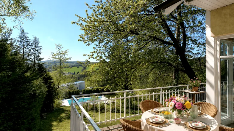 Einladender Balkon mit Esstisch, Blick auf den Garten, Pool und die grüne Hügellandschaft.