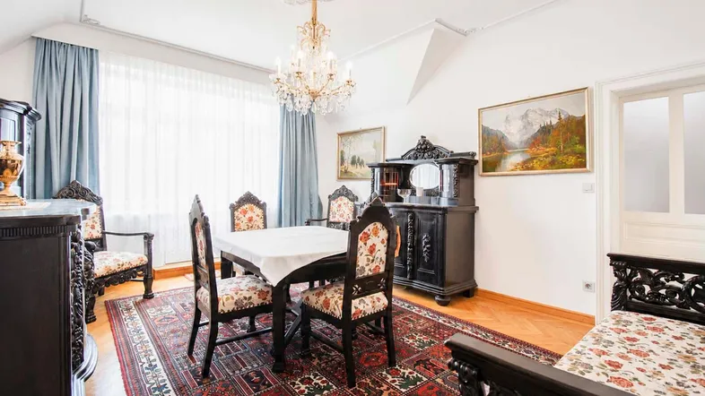 Antiker Wohn-Essbereich mit elegantem Kronleuchter, dunklen Holzmöbeln und gemustertem Teppich.