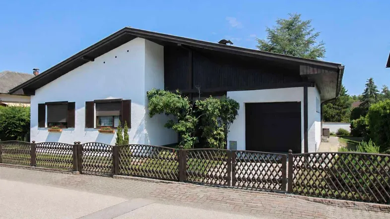 Gepflegtes Einfamilienhaus mit weißer Fassade, dunklem Dach und Vorgarten mit Zaun.
