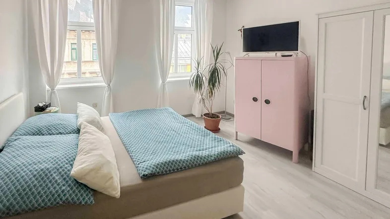 Helles Schlafzimmer mit Doppelbett, hellem Laminatboden und Blick auf die Stadt.