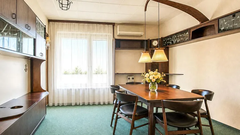 Gemütlicher Essbereich mit Holztisch, Stühlen und Blick ins Grüne durch große Fenster.