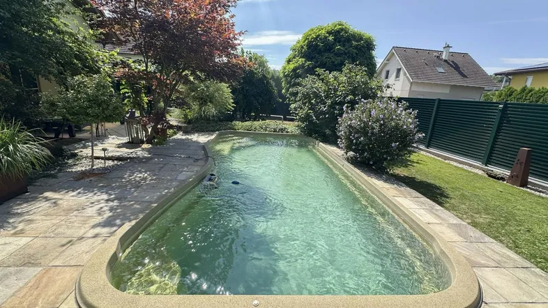 Großer Außenpool umgeben von einer gepflasterten Terrasse und üppigem Grün im Garten.