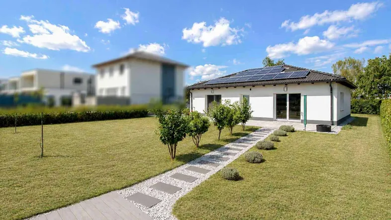 Modernes Einfamilienhaus mit gepflegtem Garten und Solaranlage auf dem Dach unter blauem Himmel.
