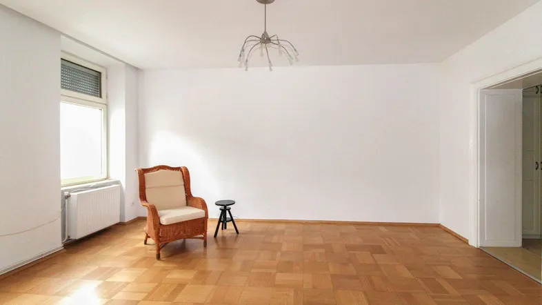 Helles Wohnzimmer mit Parkettboden und einem großen Fenster, das viel Tageslicht hereinlässt.
