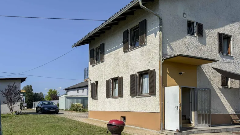 Vorderansicht des Hauses mit heller Fassade, braunen Fensterläden und einem gepflegten Vorgarten.
