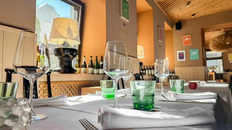 Ein gedeckter Esstisch in einem Restaurant mit Weinflaschen im Hintergrund und natürlichem Lichteinfall durch ein Fenster.