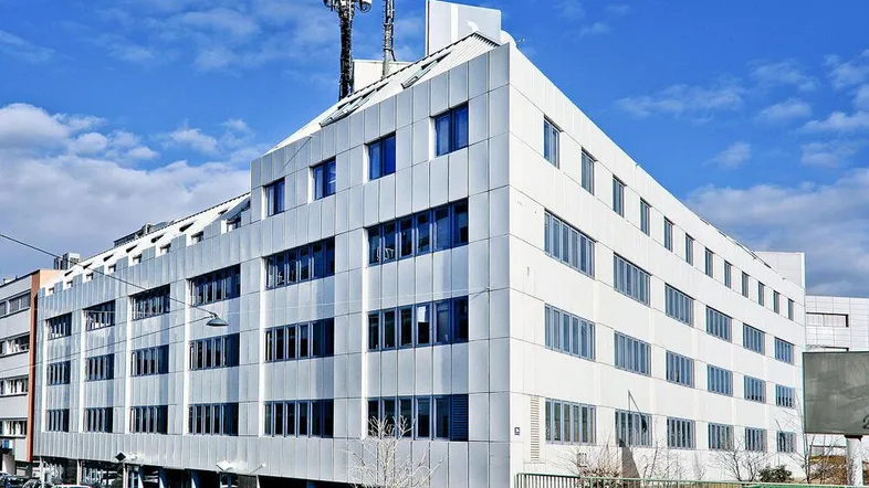 Modernes Bürogebäude mit weißer Fassade und vielen Fenstern unter blauem Himmel.