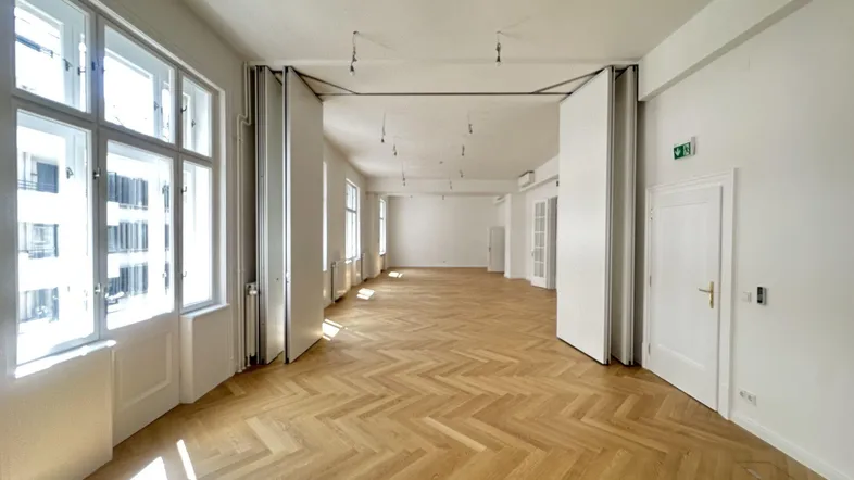 Großer, heller Raum mit Fischgrätparkett und hohen Fenstern, ideal für Büronutzung oder Veranstaltungen.
