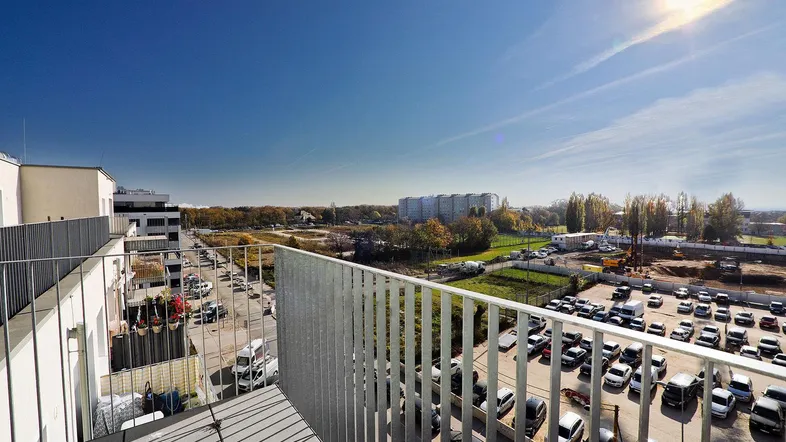 Geräumiger Balkon mit Blick auf die Umgebung und einen Parkplatz unter strahlend blauem Himmel.