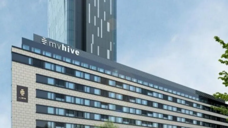 Moderne Gebäudefassade mit dem Firmenlogo "mvhive" und einem hohen Wolkenkratzer im Hintergrund.
