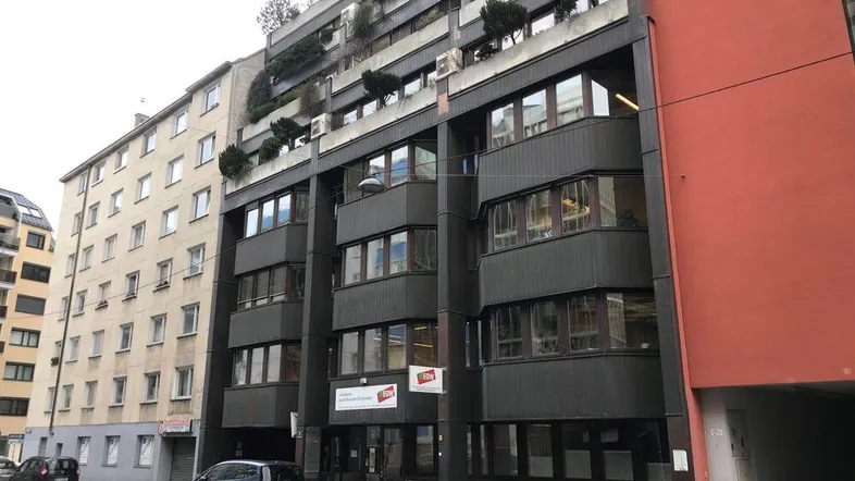 Ansicht eines modernen Bürogebäudes mit dunkler Fassade, vielen Fenstern und begrünten Balkonen.