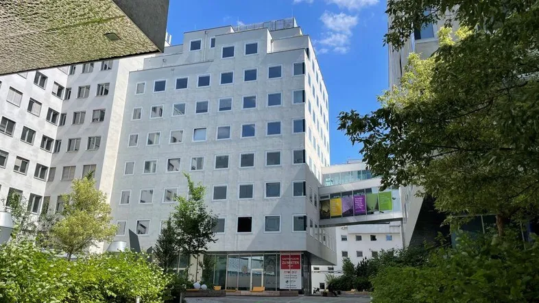 Modernes Gebäudeensemble mit weißer Fassade, vielen Fenstern und begrünten Außenbereichen unter blauem Himmel.