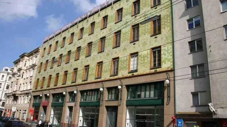 Historische Gebäudefassade mit vielen Fenstern und Geschäften im Erdgeschoss an einer belebten Straße.