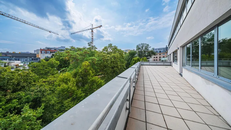 Geräumige Außenterrasse mit Fliesenboden und weitem Blick über Bäume und die Stadt.