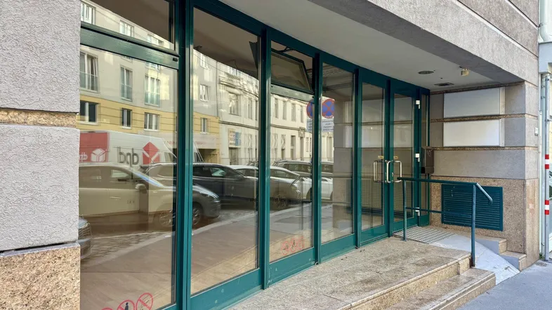 Eingangsbereich eines Gebäudes mit großen Glasfenstern und einer Rampe für barrierefreien Zugang.
