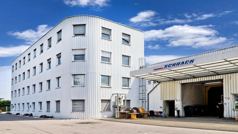 Modernes Geschäftsgebäude mit weißer Fassade und angrenzender Lagerhalle unter blauem Himmel.