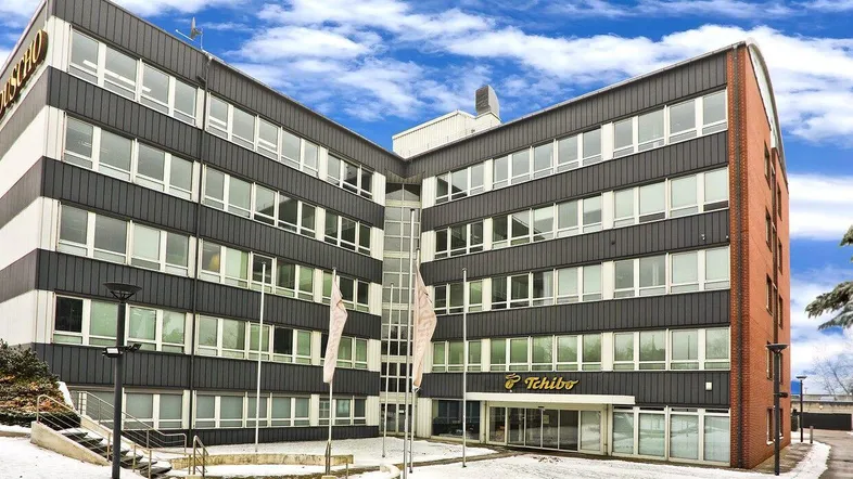 Modernes Bürogebäude mit dunkler Fassade, vielen Fenstern und einem Eingangsbereich im Winter.