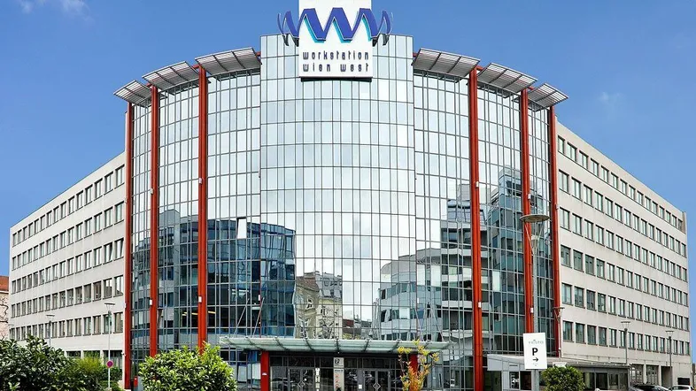 Modernes Bürogebäude mit großer Glasfassade und markantem Schriftzug unter blauem Himmel.