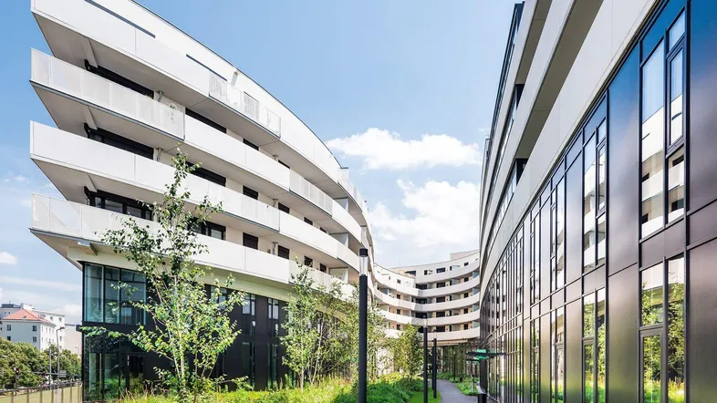 Moderne, geschwungene Wohngebäude mit Balkonen und begrünten Außenanlagen unter blauem Himmel.