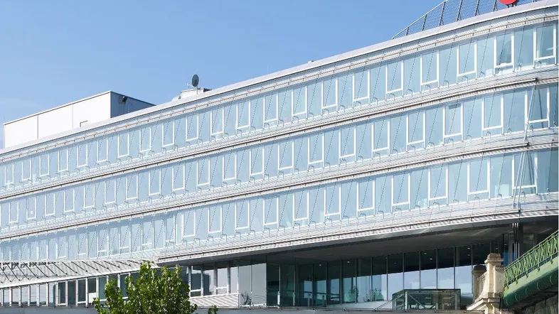 Modernes Bürogebäude mit Glasfassade und dem TUI-Logo auf dem Dach, unter blauem Himmel.