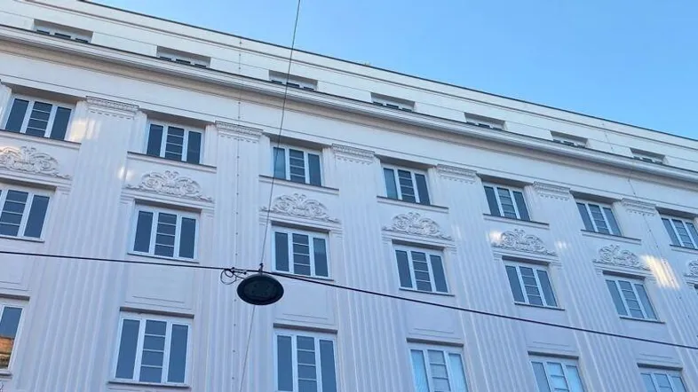 Fassade eines klassischen Gebäudes mit vielen Fenstern und dekorativen Elementen unter blauem Himmel.