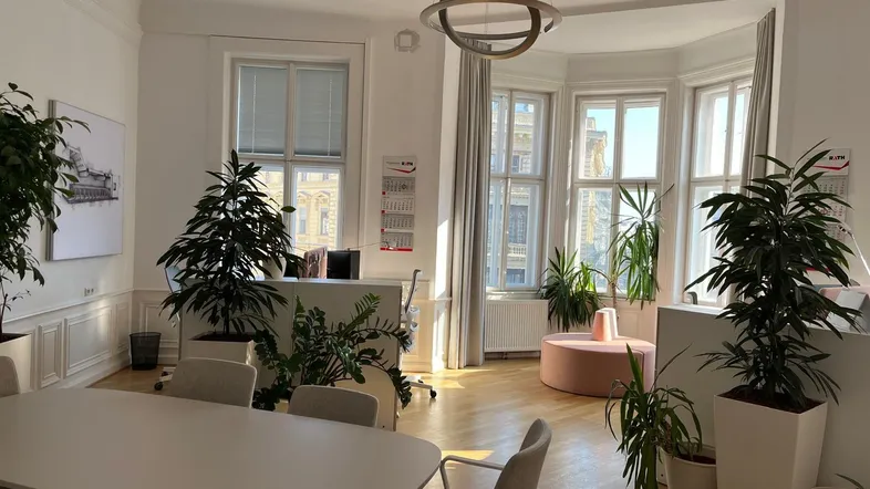 Helles und geräumiges Büro mit großen Fenstern, Holzboden und vielen Pflanzen, ideal für Besprechungen.