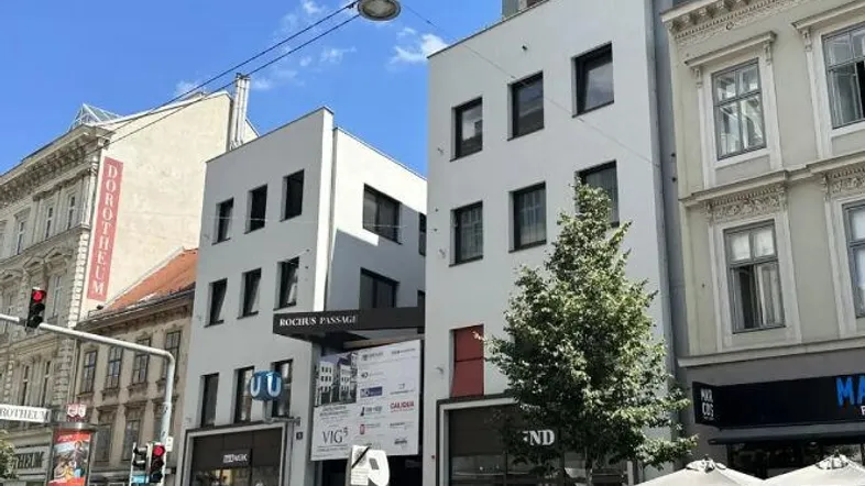 Moderne Geschäftsgebäude mit großen Fenstern und dem Eingang zur Rochus Passage in einer belebten Stadtstraße.