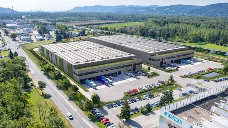 Luftaufnahme eines modernen Industriegebäudes mit Gründach und Photovoltaikanlage, umgeben von viel Grün und Parkplätzen.