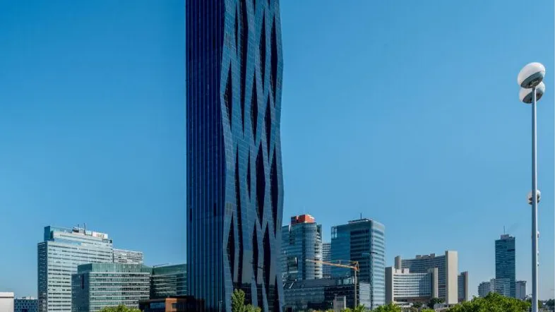 Moderner Wolkenkratzer mit markanter Glasfassade und urbaner Umgebung unter blauem Himmel.