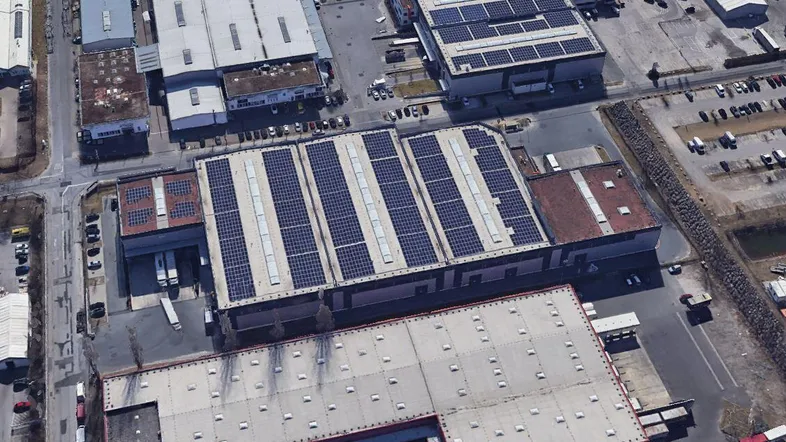 Luftaufnahme eines Industriegebiets mit mehreren Gebäuden, darunter eines mit Photovoltaikanlage auf dem Dach.