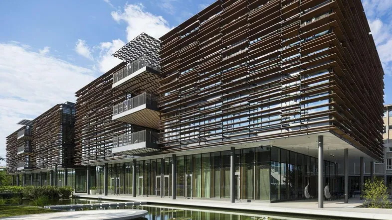 Modernes Bürogebäude mit Holzlamellenfassade, großen Glasflächen und einem Teich im Vordergrund.