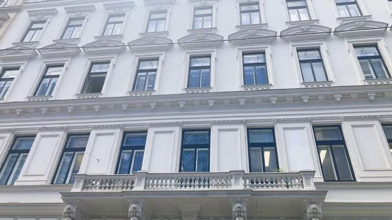 Historische Fassade eines Altbaus mit vielen Fenstern und einem verzierten Balkon im Vordergrund.