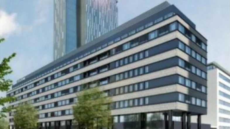 Modernes Gebäude mit dunkler Fassade und großen Fenstern, umgeben von Bäumen und Parkplätzen.