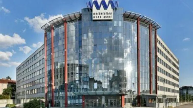 Modernes Bürogebäude mit auffälliger Glasfassade und Firmenlogo unter blauem Himmel.