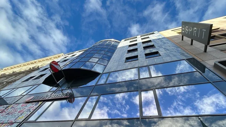 Moderne Glasfassade eines Geschäftsgebäudes, die den blauen Himmel und Wolken widerspiegelt.