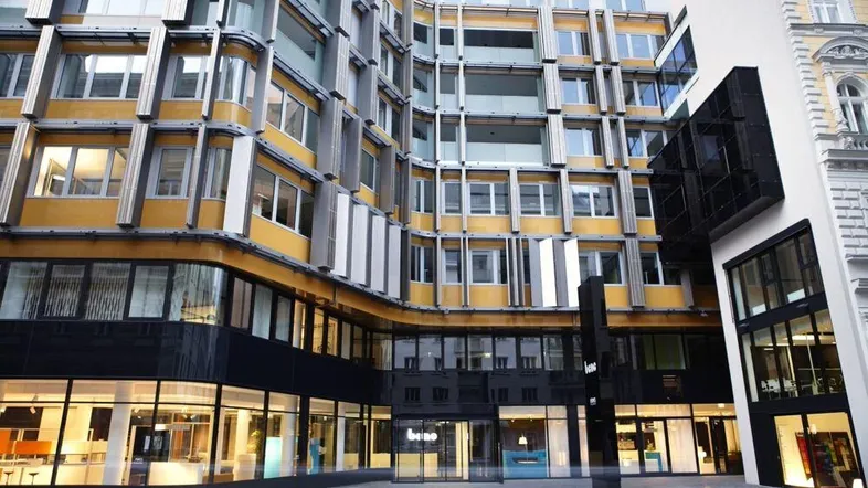 Moderne Bürogebäude-Fassade mit großen Fenstern und gelben Akzenten in urbaner Umgebung.