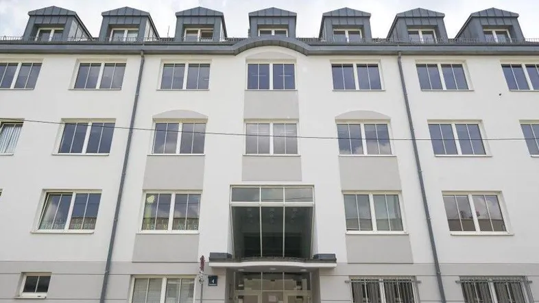 Mehrstöckiges Gebäude mit vielen Fenstern und Dachgauben unter einem bewölkten Himmel.